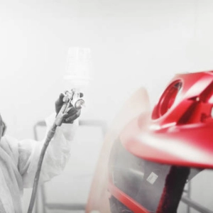 Technician spray painting a car bumper in a professional car repair shop.