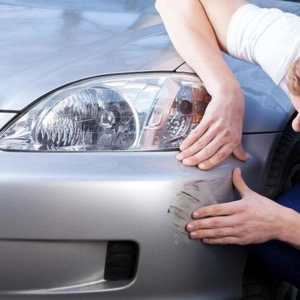 Person inspecting a scratch on a car bumper.
