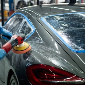 Technician polishing a car with a buffing machine in a car repair shop.